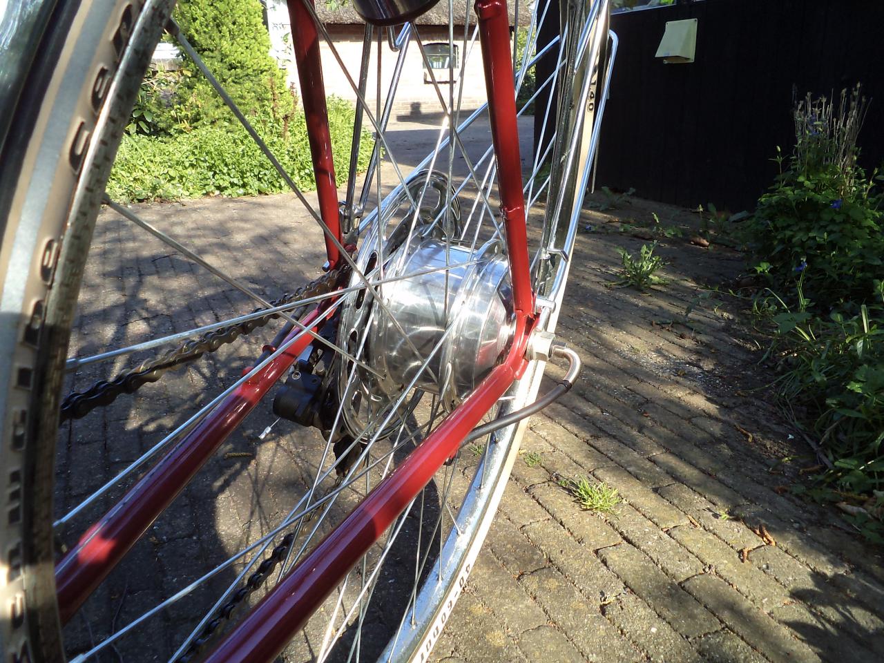 De motor in de achteras. Ik heb hem mooi glimmend gepoetst en door de spaakbeschermer valt hij niet eens zo erg op. De kabel komt er aan de linkerkant uit (voor de kijker rechts) en loopt onder de buis langs naar de bidon.